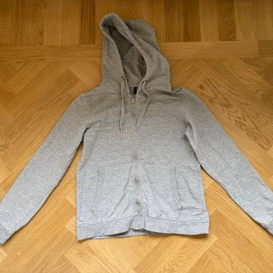 Grå zip up hoodie - Säljer en enkel grå zip up hoodie i storlek S. Tröjan har dragkedja framtill, två fickor och snörning vid huvan. Märke på bild 2.