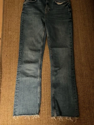 Blå raka jeans med fransig kant - Säljer ett par blå jeans från Zara med rak passform och fransig, rå kant längst ner på benen. Stolek 36 har använts några gånger.