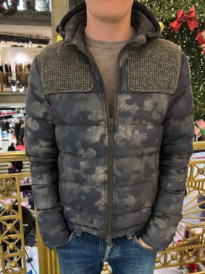 Herno jacka  - Herno vinterjacka  Stilren och lätt Herno vinterjacka i grått kamouflagemönster. Varm och vadderad med luva, hel dragkedja och en strukturerad panel över bröstet. Bekväm att bära och enkel att matcha för vardagsbruk under vintern.  Jackan är i mycket gott skick, utan hål, fläckar eller skador. Dragkedja och sömmar är helt intakta och jackan har tagits väl om hand. 