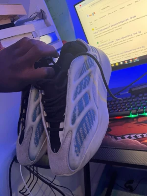 Adidas Yeezy 700 V3 blå och vita sneakers - Säljer ett par Adidas Yeezy 700 V3 sneakers i blått och vitt med svarta detaljer. Skorna har en futuristisk design med meshpaneler, syntetiska inslag och snörning. Sulan är chunky och har genomskinliga partier med blått mönster. Perfekta för dig som gillar streetwear.