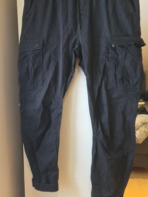 Svarta cargopants från H&M XL - Säljer ett par svarta cargopants från H&M i storlek XL. Byxorna har flera stora fickor på sidorna, slim fit-passform och är gjorda i bomull. Perfekta för dig som gillar en avslappnad men ändå stilren look.