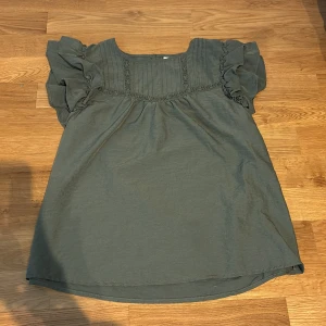 Grön blus med volangärmar  - Supersöt grön blus från JDY med volangiga korta ärmar och fina spetsdetaljer framtill. Blusen har en lös passform och rund halsringning. Perfekt för dig som gillar romantiska detaljer och en chill vibe.