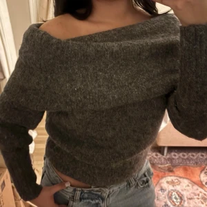 offshoulder stickad tröja  - Mysig grå stickad tröja från H&M med offshoulder-design. Tröjan har lång ärm och en bred krage som vilar snyggt över axlarna. Perfekt för att ge en chill men ändå stilren vibe till din outfit.