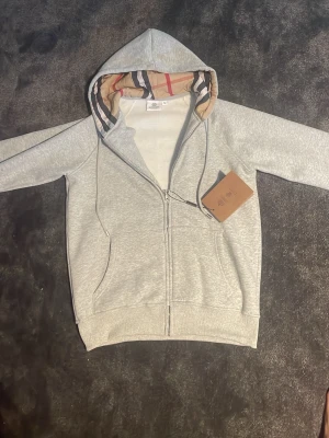 Grå burberry zip - Helt ny Burberry zip inga defekter, nytt skick och riktigt snygg dock är den väldigt liten i storlek det står L men passar S/M mer info får ni i dm