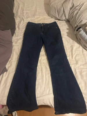 Blå bootcut jeans från Gina Tricot - Säljer ett par mörkblå jeans från Gina Tricot, modell Sabrine. De har klassisk femficksdesign, bootcut-ben och normal passform. Jeansen är tillverkade i ett mjukt bomullsmaterial med lite stretch för extra komfort. 