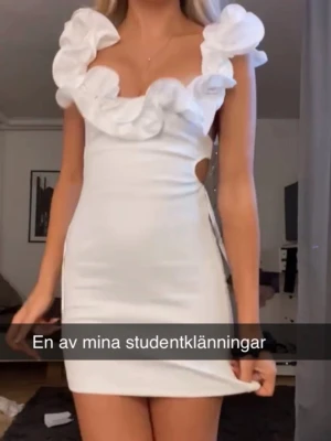 Vit volangklänning från Zara - Supersöt vit kort klänning från Zara med stora volanger runt urringningen och axlarna. Figurnära passform och öppen detalj vid sidan. Perfekt till student eller sommarens alla tillfällen. Materialet känns lätt och luftigt.