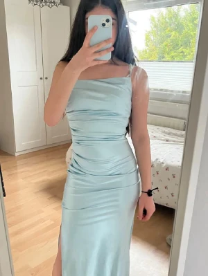 Ljusblå långklänning i satin - Supersnygg ljusblå långklänning i glansigt satinmaterial med smala axelband och slits på sidan. Skriv för mer bilder om intresserad och priset kan diskuteras