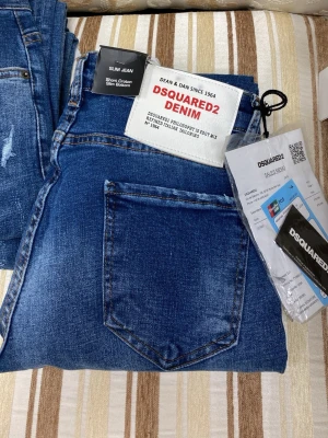 Blå slim jeans  - Säljer ett par blå slim fit jeans med snygga slitningar och klassisk femficksdesign. Jeansen har en cool washed effekt, en grön tag framtill. Perfekta för dig som gillar streetwear och vill ha något trendigt.