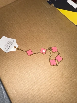 Van cleef rosa armband  - Bilderna visar ett armband med rosa blommor i rostfritt stål, inte en väst.