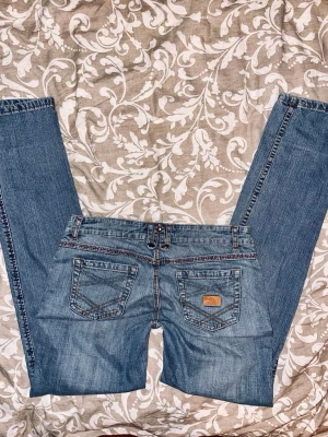 Lågmidjade jeans - Säljer ett par snygga lågmidjade jeans😍👖 De är vintage och har en rak passform i benen. De är i jättebra skick förutom att det är ett litet hål på låret, som syns på sista bilden! Storleken är 38 men jag skulle säga 36. 💞  Midjemått (rakt över): 36cm    Innerbenslängd: 80cm