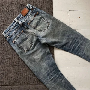 Gråa/Blåa Nudie Lean Dean Jeans - Riktigt snygga Nudie jeans med stilrena slitningar. | W30 L32. | Bra skick, bara slitningarna vid knäet har hål igenom, men man ser fof knappast ej igenom (se sista bilder). | Längd: 106cm, Midja: 37-41cm. | Pris ej hugget i sten, skriv vid minsta fundering.
