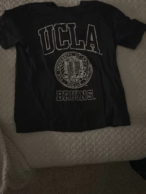 Svart UCLA t-shirt från H&M XS - Snygg svart t-shirt från H&M i storlek XS med stort vitt UCLA-tryck och Bruins-logga på bröstet. Klassisk rund hals och korta ärmar. Perfekt för dig som gillar college-vibe och vill sticka ut lite extra.