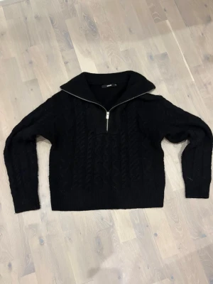 Svart stickad half zip tröja BikBok - Svart stickad tröja från BikBok i storlek XS. Tröjan har ett snyggt kabelstickat mönster, hög krage och half zip-dragkedja framtill. Långärmad och med ribbade muddar vid ärmslut och nederkant. Perfekt för kyliga dagar.