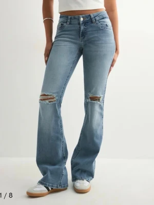 Bootcut jeans med slitningar från Nelly - Snygga ljusblå bootcut jeans från Nelly med slitna detaljer över knäna och dekorativa sömmar på bakfickorna. Jeansen har normal passform. Perfekta för dig som gillar en avslappnad men trendig look. Fick i julklapp och passade ej och försent för att lämna tillbaks! Nypris 699kr