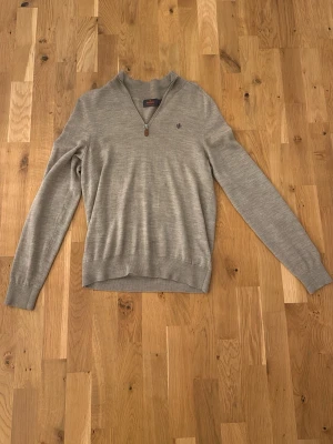 Ljusbrun merinoulltröja från Morris - Snygg ljusbrun långärmad tröja från Morris i 100% merinoull. Tröjan har half zip med läderdetalj och en liten broderad logga på bröstet. Perfekt för lager-på-lager och passar till både jeans och chinos.