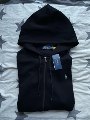 Polo Ralph Lauren kofta – Ny med tag - Polo Ralph Lauren kofta med mörkgrå logga.  Koftan passade tyvärr inte och har därför inte kommit till användning.  Skick: oanvänd / nyskick.