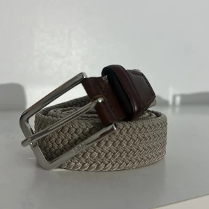Flätat Hugo boss bälte - Snyggt och exklusivt Hugo Boss-bälte i flätad textil med detaljer i brunt läder och silverfärgat spänne. Passar lika bra till vardag som till finare tillfällen.