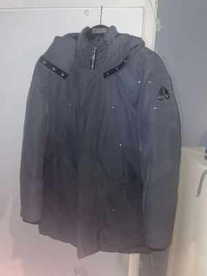 Moose Knuckles cloud 9 jacka M - Säljer en grå dunjacka från Moose Knuckles med huva och svarta detaljer. Jackan har flera fickor, dragkedja framtill och logga på ärmen. Insidan är svart och quiltad för extra värme. Perfekt för kalla dagar, pris kan diskuteras, Jackan är köpt 2023 vinter. Knappt använd.