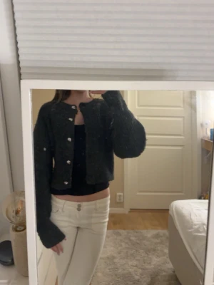 Mörkgrå kofta från H&M - Säljer en mysig mörkgrå kofta från H&M i storlek XS. Koftan är stickad med fluffig struktur, har långa ärmar och knäpps med silvriga knappar framtill. Perfekt för lager på lager och chill dagar.