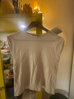 Vit ribbad ärmlös topp från Zara - Säljer en enkel och clean vit topp från Zara i storlek S. Toppen är ribbad, har rund halsringning och är ärmlös vilket gör den perfekt till sommaren. Materialet känns mjukt och stretchigt.