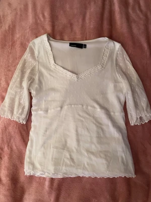 Vit spetsblus från KappAhl - Söt vit blus från KappAhl med v-ringning och spetsdetaljer runt halsen. Ärmarna är trekvarts och i tunn mesh med små broderade blommor. Blusen har lätt volangkant nedtill och är i ett mjukt, tunt material som känns luftigt.😊