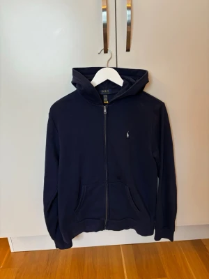 Polo Ralph Lauren Zip Hoodie strl 18-20 -  Säljer en Polo Ralph Lauren hoodie med zip i bra skick. Finns en liten fläck på framsidan av tröjan men den syns inte mycket. Annars är den i bra skick. Säljer den för att den är för liten.