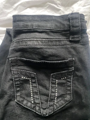 Svarta jeans med nitar från Gina Tricot - Svarta jeans från Gina Tricot med snygga nitar på bakfickan som ger extra edge. Klassisk femficksmodell med dragkedja och knapp framtill. Jeansen har smal passform och är gjorda i stretchigt bomullsmaterial för skön känsla. Bootcut och lowwaist, storlek S (Fast från young)