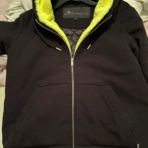 Svart teddyjacka Moose Knuckles L - Svart teddyjacka från Moose Knuckles i storlek L med mjukt limegrönt foder och quiltad insida. Jackan har dragkedja, huva med snörning och stora fickor framtill. Snygga metall-logodetaljer på ärmen ger extra edge.