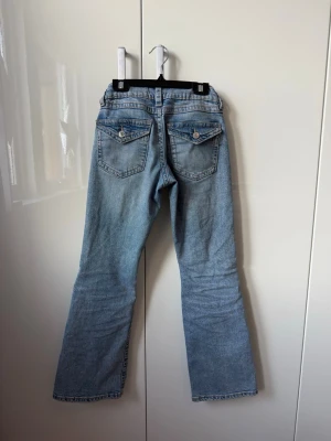 Bootcut ljusblå jeans med slitningar - Säljer ett par ljusblå bootcut jeans ifrån Gina tricot jeans med slitningar på knäna och knappar på fickorna. Jeansen är i storlek 152 och är low waist med justerbar midja💗