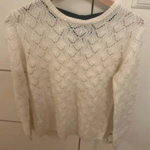 Vit stickad tröja med rosett - Supersöt vit stickad tröja med lång ärm. Tröjan har en svart rosett på baksidan som en extra detalj. Perfekt för dig som gillar en romantisk och mysig stil. 