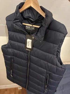Mörkblå väst från Indicode - Säljer denna snygga mörblå väst från indicode. Den är helt ny och har kvar pris taggen. Den är snygg och enkel att matcha till olika outfits. Säljer för billigt pris.
