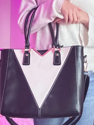 Väska . Svart och vit handväska med guldiga detaljer - Snygg handväska i svart och vitt med coolt V-format mönster framtill. Väskan har två rejäla handtag och en avtagbar axelrem med guldiga metalldetaljer. Materialet är slätt skinnimitation och insidan är rymlig för allt du behöver ha med dig. Perfekt för dig som gillar stilrena kontraster.