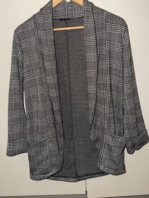 Grå rutig kavaj med fickor - Snygg grå kavaj med klassiskt rutigt mönster och öppet framtill. Jackan har två stora fickor och uppvikta ärmar som ger en chill vibe. Perfekt för att lyfta din outfit med lite extra stil. Passar dig som gillar en loose fit och vill ha något som sticker ut.