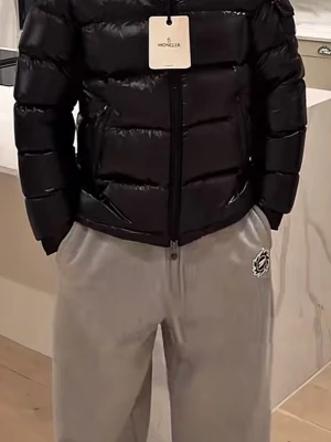 Svart Moncler pufferjacka - Säljer en svart pufferjacka från Moncler med glansig finish och horisontella sömmar. Jackan har huva, två snedställda fickor med dragkedja och Moncler-logga på ärmen. Perfekt för kalla dagar och har en riktigt modern vibe. Äkta!