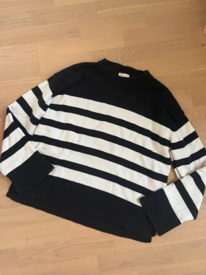 Randig svartvit stickad tröja - Säljer en svart och vit randig stickad tröja med breda muddar och rund hals. Tröjan har lång ärm och en relaxed fit som passar perfekt till jeans eller kjol. Klassisk och enkel design som aldrig går ur tiden.