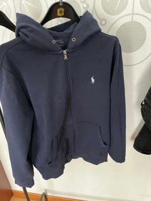 Ralph Lauren full zip, med luva - Polo Ralph Lauren full zip med luva, i marinblå. Den säljes utan snören då det enligt mig ser bättre ut. 