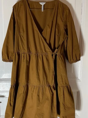 Kakifärgad omlottklänning från Object - Säljer en mörkbeige/kakifärgad midiklänning från Object i storlek 38. Klänningen har omlottmodell med knyt i midjan, volangdetaljer och trekvartsärmar med resår. Tillverkad i mjuk bomull som känns skön mot huden. Perfekt för dig som gillar en avslappnad men uppklädd stil. Mått: byst: 55 cm midja: 52cm längd: 90 cm. Djur finns i hemmet. Inga synliga fel. 
