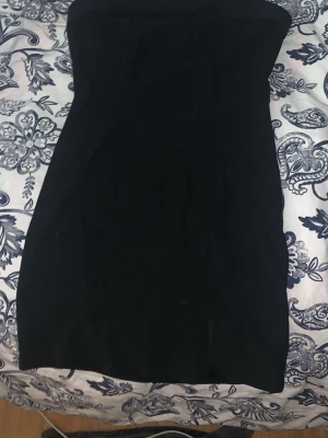 Svart axelbandslös kortklänning - Säljer en svart axelbandslös kortklänning med enkel och stilren design. Klänningen har en tight passform och är perfekt för dig som gillar minimalistisk stil. Materialet känns mjukt och följsamt mot kroppen. Perfekt att styla med smycken eller en cool jacka.