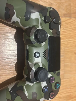 PlayStation DualShock 4 Camo Edition - Snygg PlayStation DualShock 4 handkontroll i camo-design. Kontrollen har touchpad, vibrationsfunktion och klassiska PlayStation-knappar. Några mindre repor och tecken på användning syns, men överlag i gott skick. Perfekt för dig som vill ha en unik och pålitlig spelupplevelse. Pris kan diskuteras 
