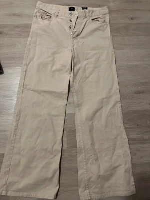 Beige wide loose fit byxor från H&M - Snygga beige byxor från H&M i loose fit med wide ben och klassisk femficksdesign. Byxorna har knappar i gylfen och är tillverkade i mjuk bomull. Perfekt för dig som gillar avslappnad stil och breda ben.