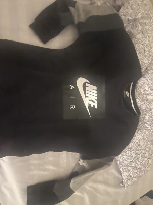 Svart Nike Air sweatshirt - Svart sweatshirt från Nike Air med stort vitt logotryck på bröstet. Tröjan har rund hals och långa ärmar med gråa paneler. Perfekt för dig som gillar sportig och clean streetstyle. Materialet är mjuk bomull och polyesterblandning.