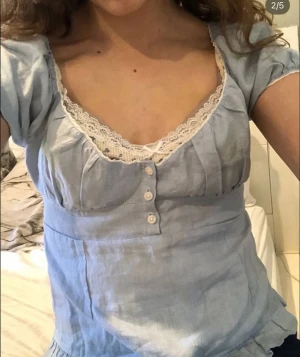 brandy blus blair - Supersöt ljusblå blus med kort ärm, knappar framtill och vacker vit spets längs urringningen. Tröjan  har en feminin passform och är gjord i ett lätt material som känns perfekt för varmare dagar.