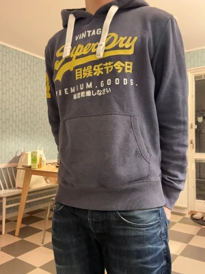 Superdry Vintage hoodie - Sjukt fet superdryhoodie med en riktigt bra färgkombination😮‍💨Trycket på framsidan är i riktigt bra skick utan några sprickor. På axeln är trycket lite sprucket, blir en perfekt combo mellan vintage och nytt. 🤩Passformen är riktigt bra och längden är perfekt för någon mellan 175 och 180. Storlek M (finns ingen storlekslapp). Riktigt skön hoodie att ha på sig och stylas extra fint med ett par jeans som på bilden enligt mig! På bilden är jag 176cm lång. Var inte rädda att ställa frågor!😁