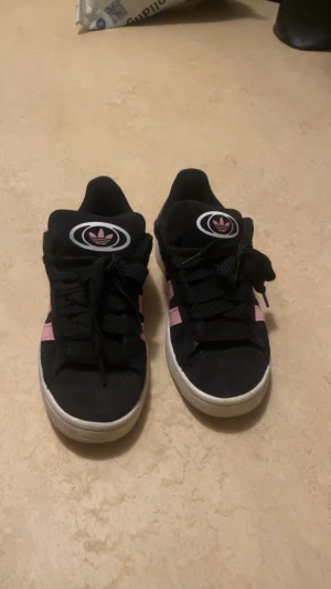 Adidas campus  - Säljer ett par svarta Adidas campus med  rosa ränder på sidorna och vit sula. Adidas logga syns både på plös och häl. Storlek 38, 2/3. Köpta för 900kr å säljs för 600kr (pris kan diskuteras) Perfekta för dig som gillar en stilren look. (Skorna går att tvätta så kan tvätta innan köp så de ser rena å nya ut) 🤗🤗