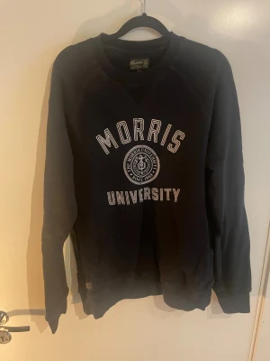 Mörkblå  Morris University sweatshirt S - Mörkblå sweatshirt från Morris med stort vitt tryck 'Morris University' och emblem på bröstet. Klassisk rund hals och långa ärmar, tillverkad i mjuk bomull.