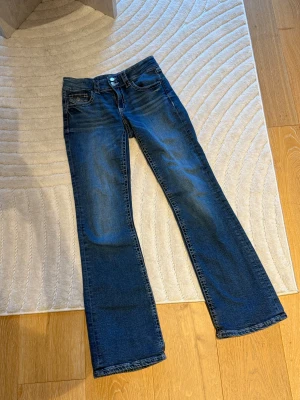 Lågmidjade blå jeans  - Säljer dessa jeans som är från gina young. Dom är i bra skick och syns inte att de har varit använda. De har två knappar på framsidan och band på sidan ifall man vill göra midjan mindre. Dom är i storlek 164, men passar lika bra som xs. 