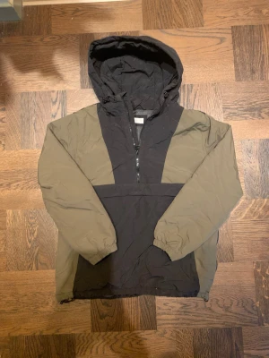 Svart och olivgrön vindjacka från MNG - Säljer en snygg vinterjacka från MNG i svart och olivgrönt med huva och half zip framtill. Jackan har elastiska muddar vid ärmslut och två fickor på sidan. Luvan och bottendelen går även att spänna åt. Sedan på vänster sida finns en lång dragkedja. Vid frågor, hör av dig? 