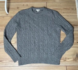 Grå kabelstickad tröja från Gap - Kabelstickad grå tröja från Gap i storlek M. Tillverkad av 55% lammull och 45% nylon, vilket gör den både mjuk och varm. Tröjan har rund hals, ribbade muddar och långärmad passform. Perfekt för dig som gillar klassisk stil med lite extra struktur.☺️