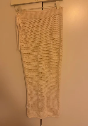 Vit stickad långkjol med snörning - Säljer en vit stickad långkjol med snyggt hålmönster och snörning i midjan. Kjolen har en loose passform och är perfekt för dig som gillar en chill och trendig stil. Passar till sneakers eller sandaler för en cool look.