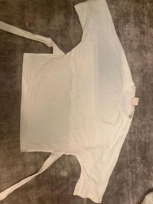 Vit omlottopp med knytband - Säljer en stilren vit omlottopp från NA-KD med korta ärmar och breda knytband i midjan. Toppen har en rak och loose passform, rund halsringning och är gjord i mjuk bomull. Perfekt för dig som gillar minimalistisk och clean stil.